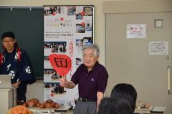 写真：素隠居の団扇を持って実演する素隠居保存会　大賀顧問